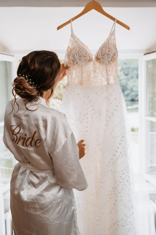 Noiva de robe olhando o vestido pendurado na janela