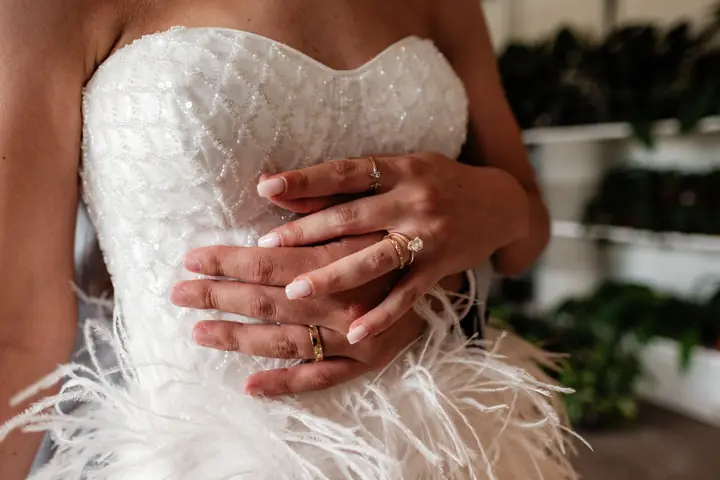 Mãos da noiva com o anel sobre o vestido de plumas