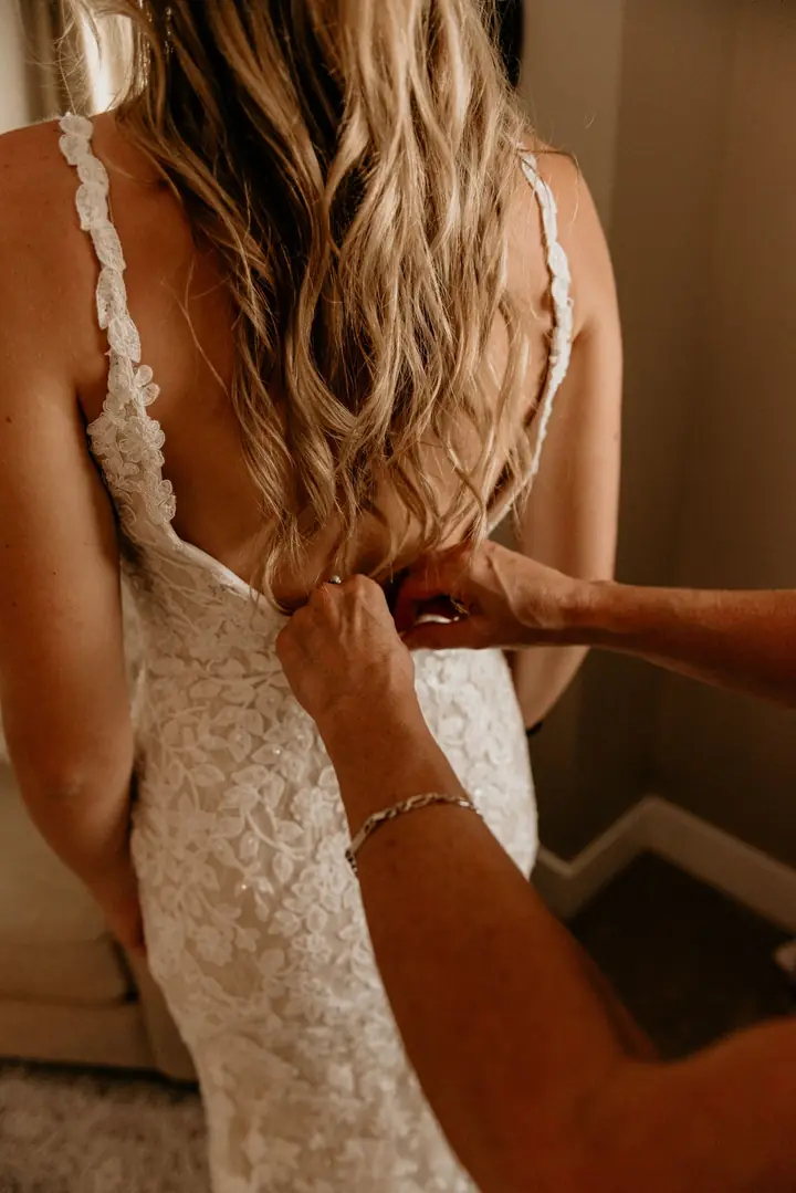 Mãos fechando o vestido de renda da noiva