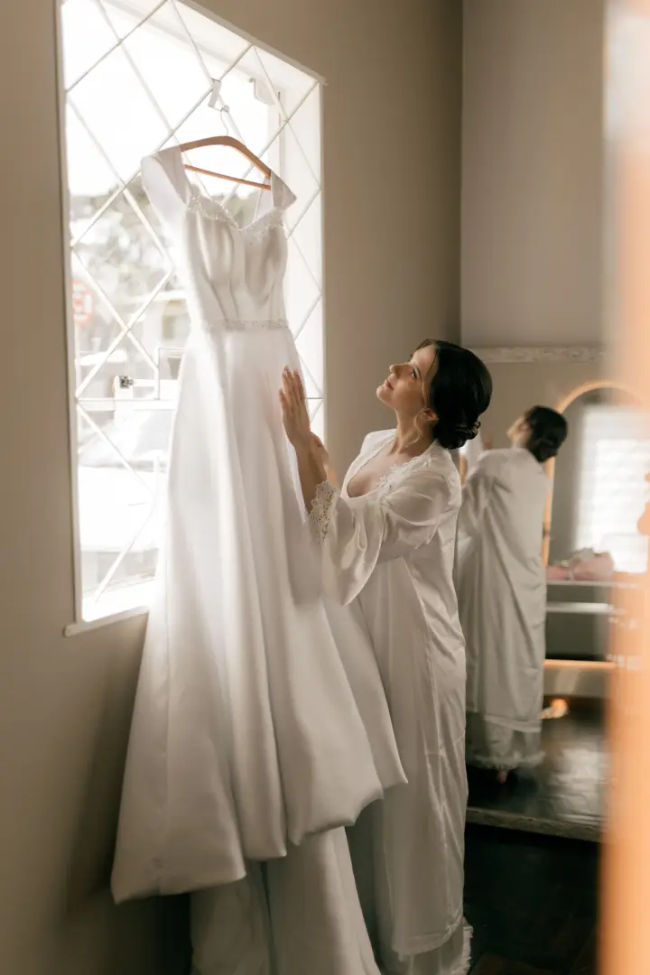 Noiva olhando o vestido pendurado na janela