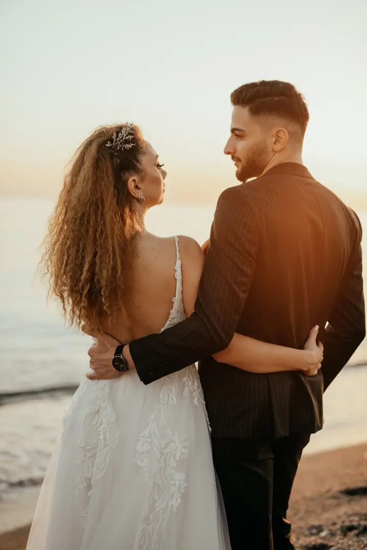 Casal abraçado na areia, olhando o mar