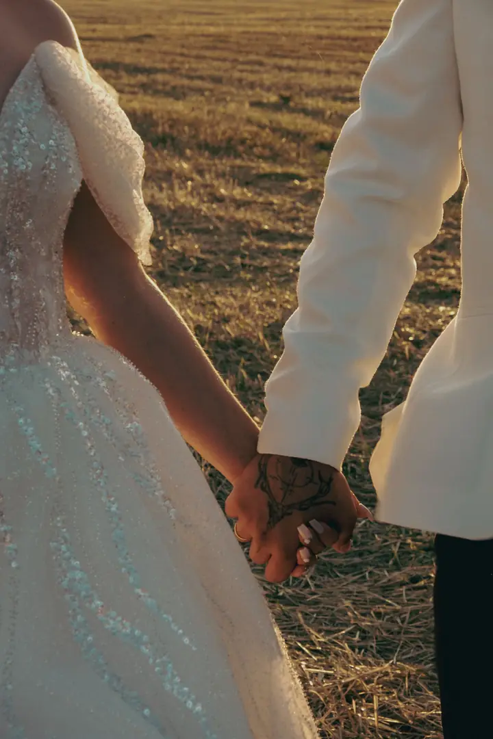 Mãos do casal entrelaçadas, vestido bordado em close